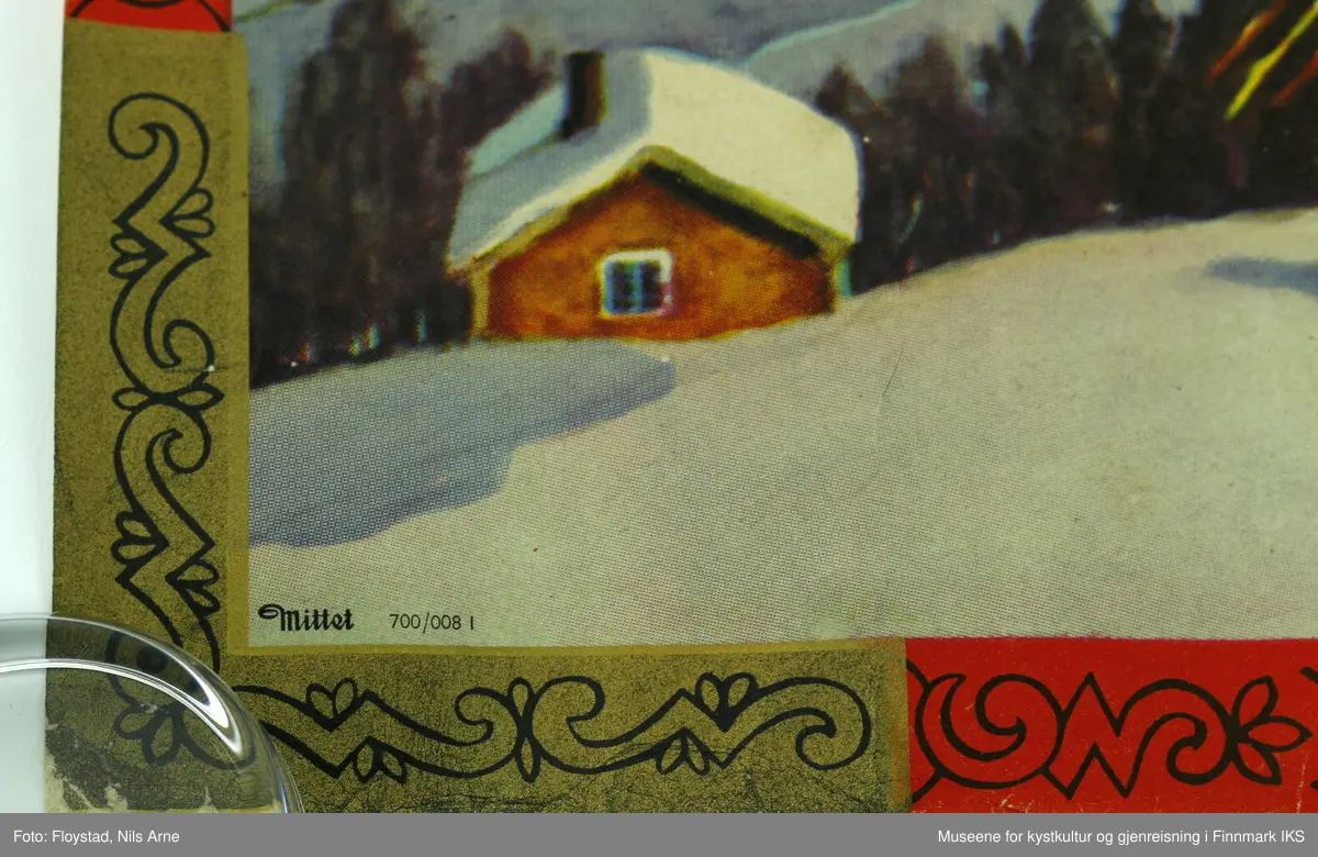 En rektangulær papirplakat med påtrykt vintermotiv av en snødekt fjellgård, et tre med julenek og fugler, en person med hest og slede. I bakgrunnen er det flere andre fjellgårder omgitt av skog og høye fjelltopper. Plakaten har en rød og gullfarget kant med mønsterdekor. Nederst i venstre hjørne står "Mittet 700/008 I", og i høyre hjørne står det "printed in Norway".