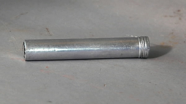 a-b) är en aluminiumburk med skruvlock. c) är glasampull med gummikork iöppningen. Rosa etikett på burken: "Nr. 3 Astra steril catgut, Typ T bruksfärdig ca. 2,5 meter, Astra, Södertälje."