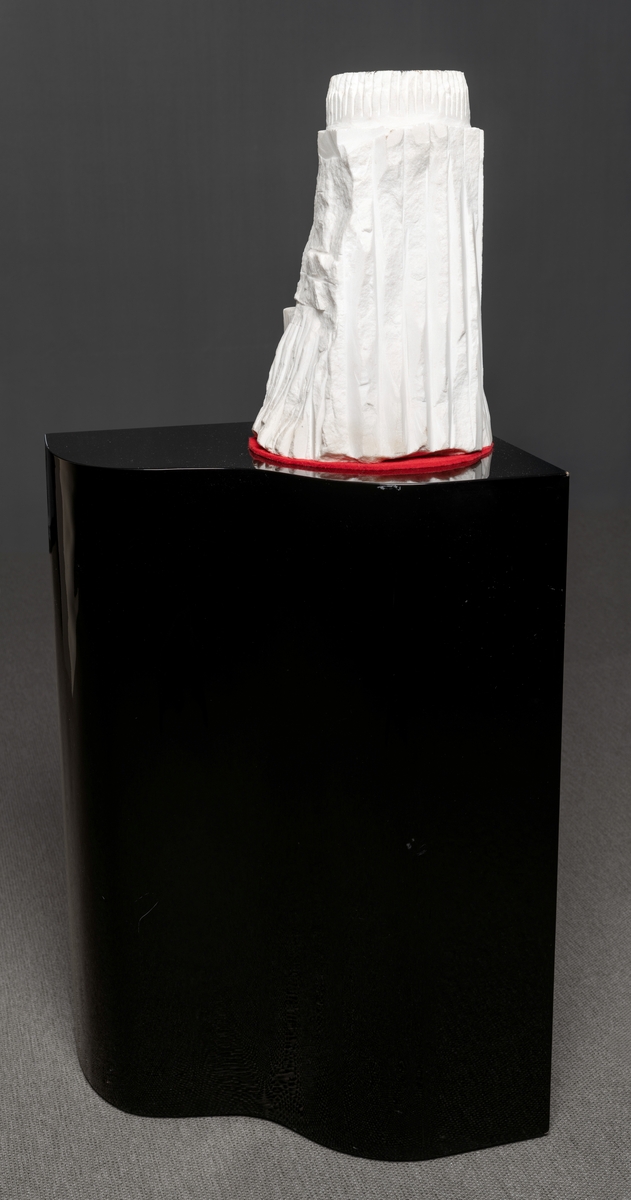 Skulptur med sokkel.
Hvit skulptur i stein på svart sokkel i lakkert tre