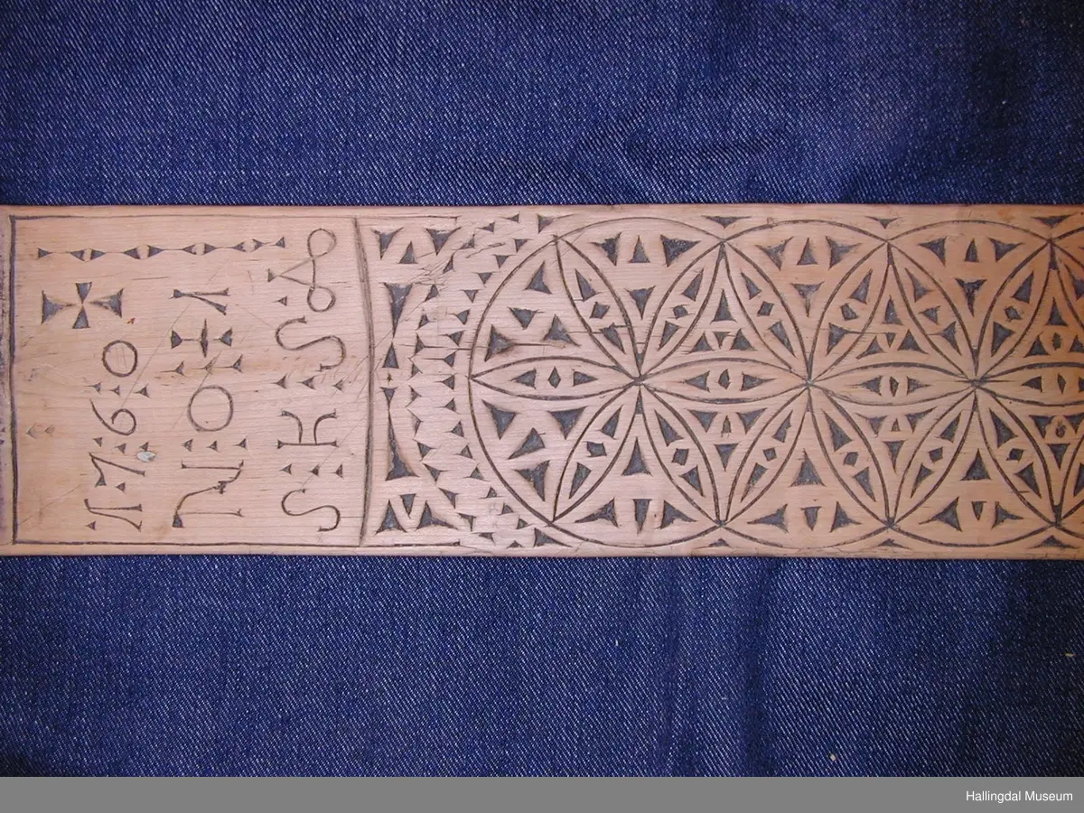 Mangletre, skore. Rektangulært tverrsnitt i sjølve fjøla, litt boga på undersida. På oversida skoren ornamentikk. På framenden på fjøla skore ein slags krok til å halde i. I attaste enden skore ein hest, felt ned i fjøla. Ytst i denne enden ei lærrreim festa med to naglar.