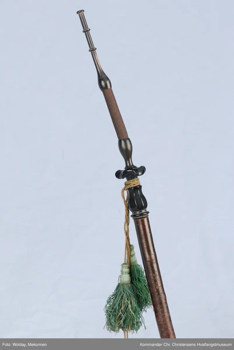 Langpipe med mellomstykke (holk) og lokk i sølv. Grønn snor med to dusker.