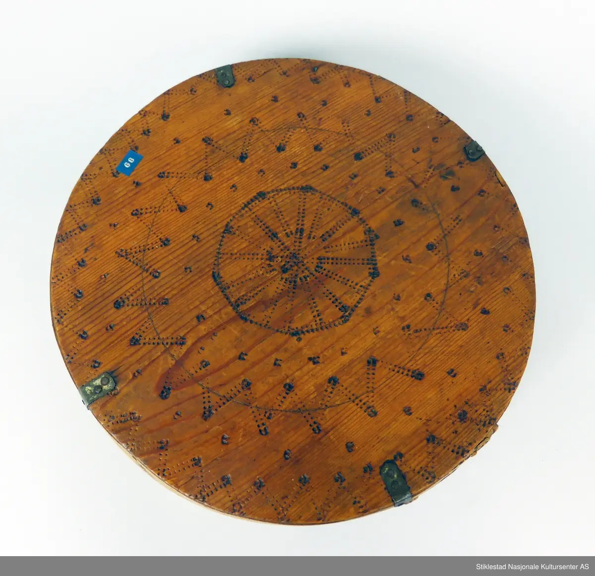 Sveipet øskje med søm av bjørketæger. Innbrent dekor på lokk og sider, rutemønster på side og lokk, 8-kant stjerne. Lokket er forsterket med vinkler av jernblikk. Trenaglene er erstatt med jernstifter