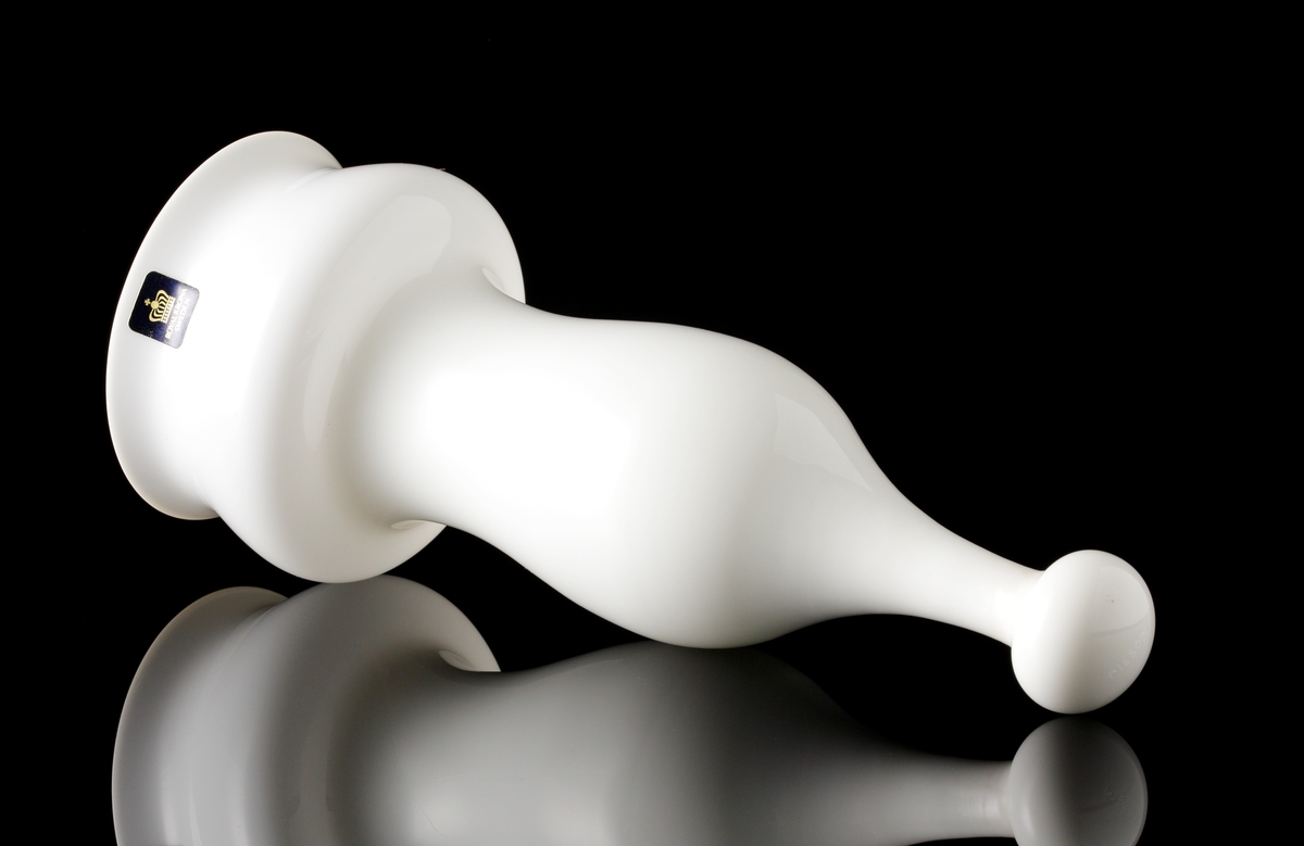 Formgiven av Bo Borgström. Vas i vitt opakt glas, ämnad att hänga på vägg. Hänganordningen i metall saknas. Mörkblå etikett med guldtext "ROYAL KRONA SWEDEN".