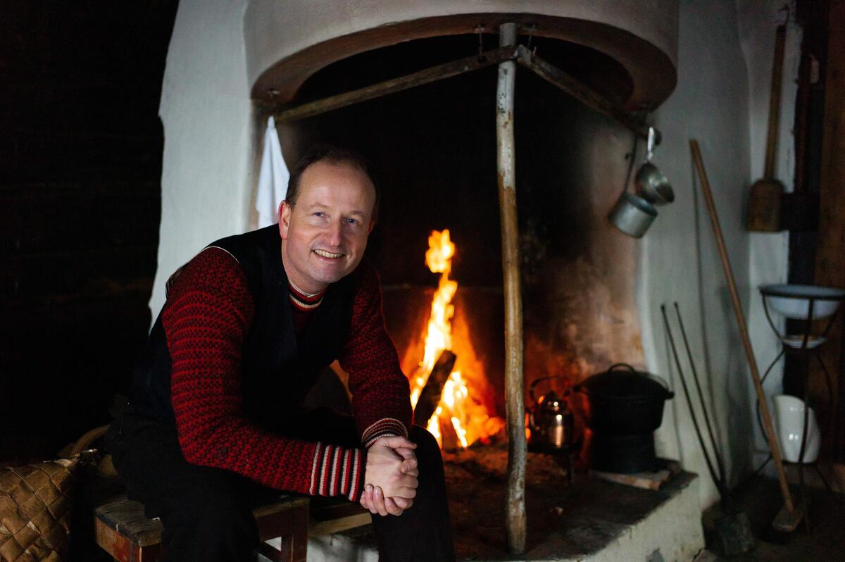 Førstekonservator Bjørn Sverre Hol Haugen sitter foran et åpent ildsted