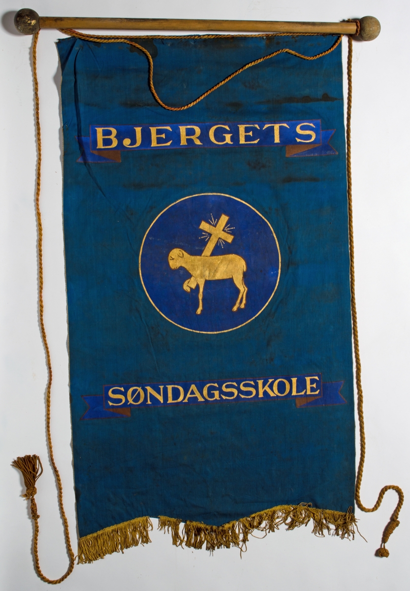 Blå faneduk i bomullslerret med tre korte tunger kantet med frynser nederst. Motiv, påskrift og frynser i gull. 

Framside: Sentrert motiv av Guds lam som bærer korset i sirkel.
Bakside: Sentrert motiv av Guds lam som bærer korset i sirkel.