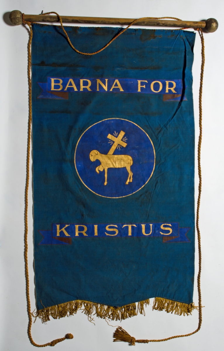 Blå faneduk i bomullslerret med tre korte tunger kantet med frynser nederst. Motiv, påskrift og frynser i gull. 

Framside: Sentrert motiv av Guds lam som bærer korset i sirkel.
Bakside: Sentrert motiv av Guds lam som bærer korset i sirkel.