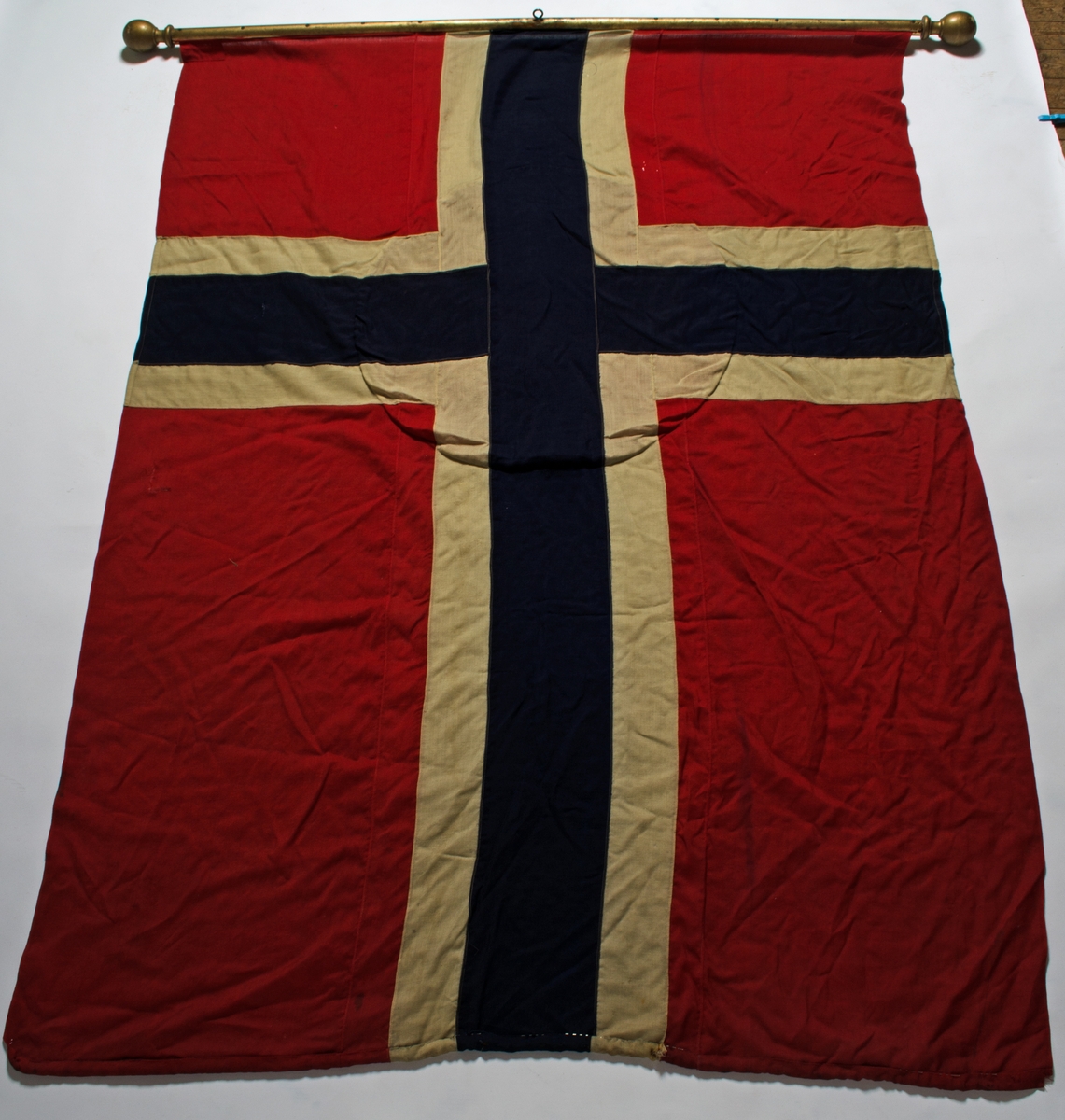 Faneduk i ull, norsk flagg i rødt, hvitt og blått med påsydd sirkel med tekst og dekor. På baksiden er det ikke påsydd sirkel med tekst og dekor. Faneduken er montert på tverrstang med kule i hver ende, to styresnorer og en bardunsnor.