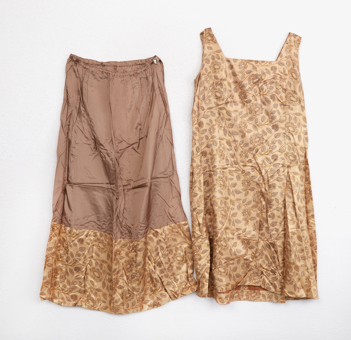 Klänning, ärmlös. Av ljusbrunt blankt tyg med tryckt mönster, blommor och blad. Kvadratisk halsringning. Dragkedja mitt bak, rosett vid halsringningen.
Underkjol med klänningstyget nedtill. 
Jacka av samma tyg som klänningen. Krage. 3/4 ärm. En knapp vid kragen. Baktill två löst hängande tygstycken, 'skört'. Fodrad med ljusbrunt tyg.
Märkt: 'Rosander'.