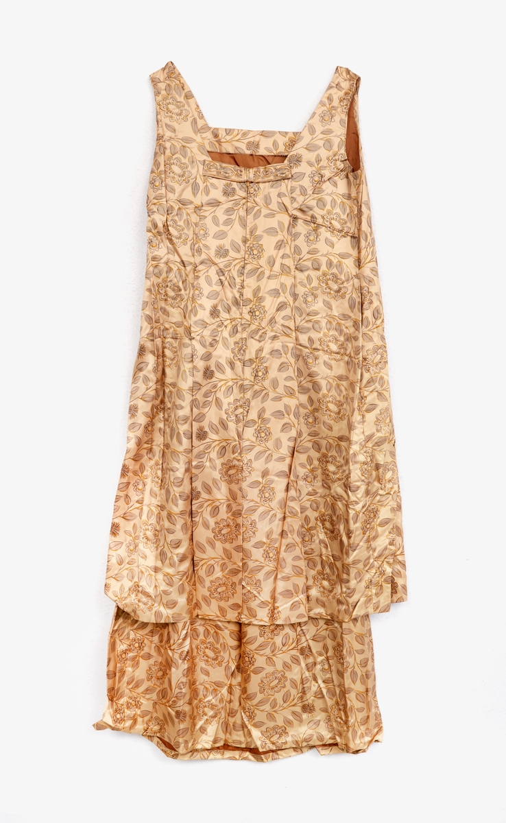 Klänning, ärmlös. Av ljusbrunt blankt tyg med tryckt mönster, blommor och blad. Kvadratisk halsringning. Dragkedja mitt bak, rosett vid halsringningen.
Underkjol med klänningstyget nedtill. 
Jacka av samma tyg som klänningen. Krage. 3/4 ärm. En knapp vid kragen. Baktill två löst hängande tygstycken, 'skört'. Fodrad med ljusbrunt tyg.
Märkt: 'Rosander'.