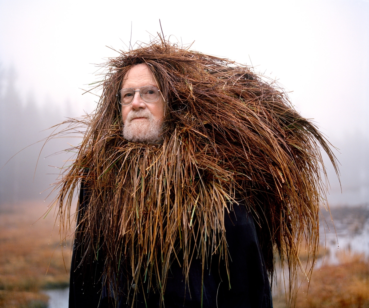 Bengt står i et disig landskap med vegetasjon fra bakken rundt hodet. Bildet er en del av serien "Eyes as Big as Plates".