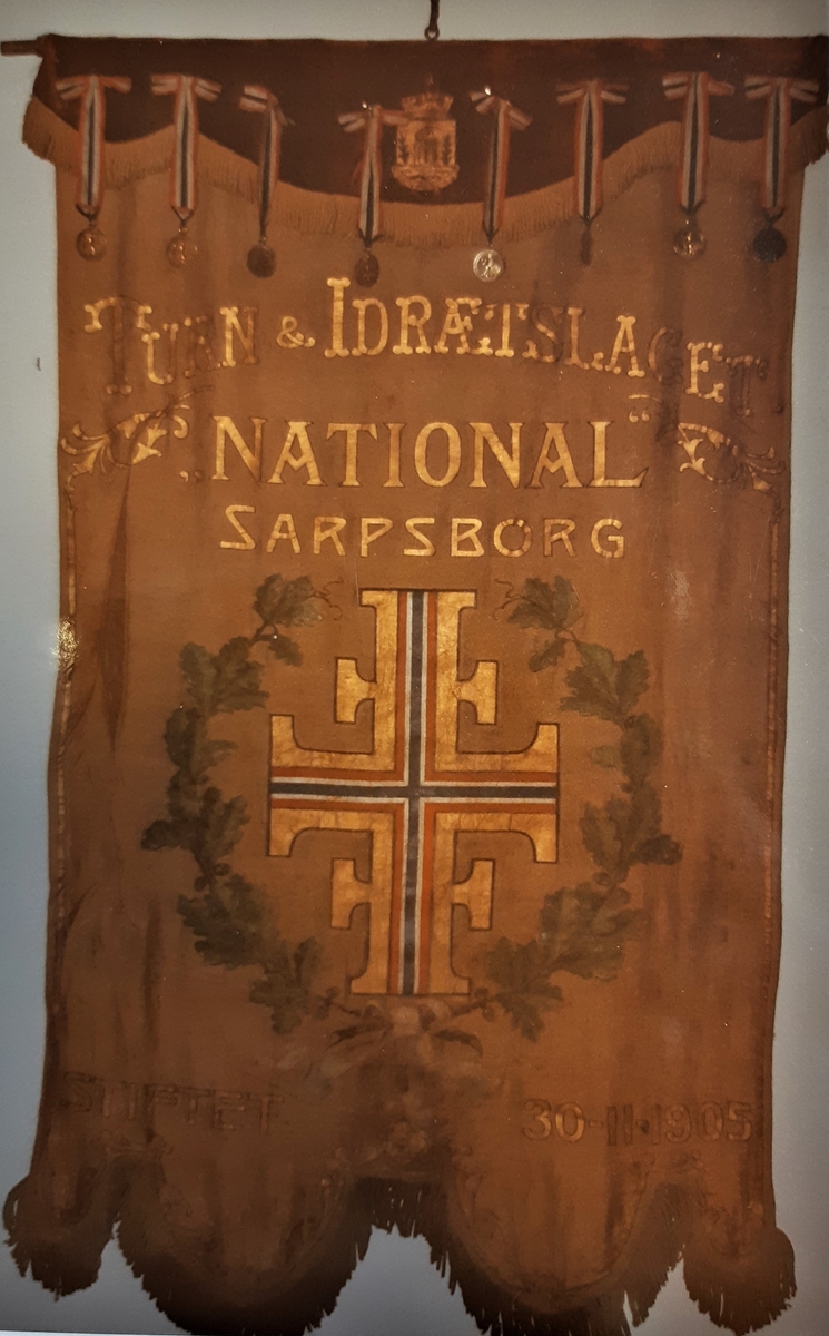 Forside: tekst, eikeløvkrans "turnlogoen" (de 4 F`er). 
Bakside: Mann (gutt) med spyd, laurbærkrans med norsk bånd, samt vektstand og kule.