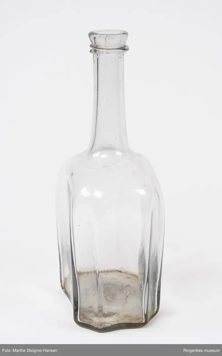 Glassflaske med lang og smal hals, brede skuldre og åttekanta form nederst på kroppen.