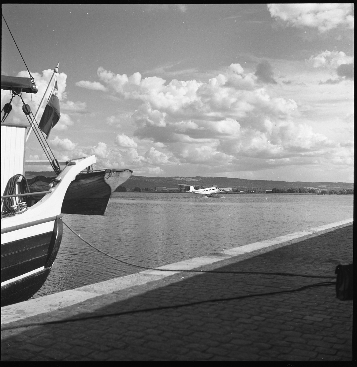 Fartyg vid kajkant, aug 1950. Okänt var men troligen i Jönköpingsområdet. Ute i sjön syns också ett flygplan.