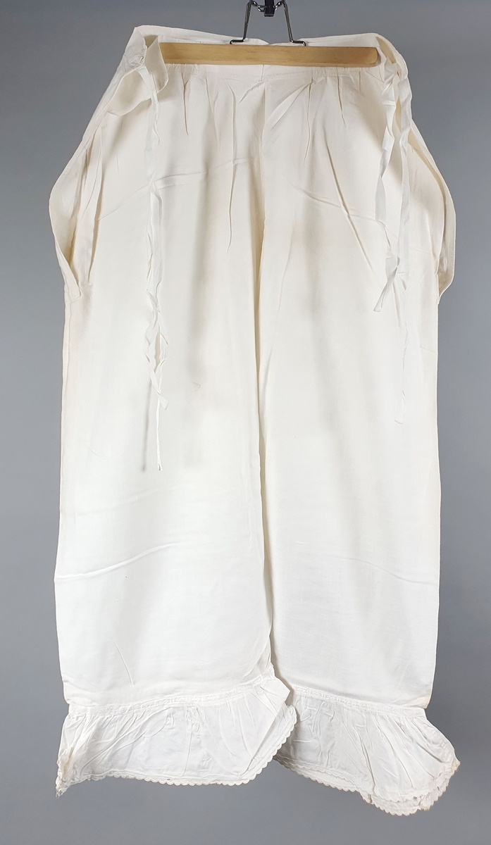 Ni like mamelukker med foldekant med bølget kant nederst.  Åpning i hver side med knytebånd.