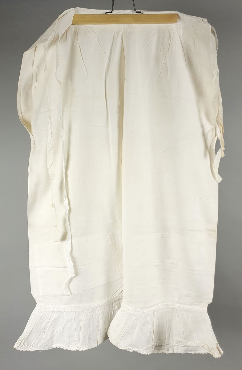 Ni like mamelukker med foldekant med bølget kant nederst.  Åpning i hver side med knytebånd.