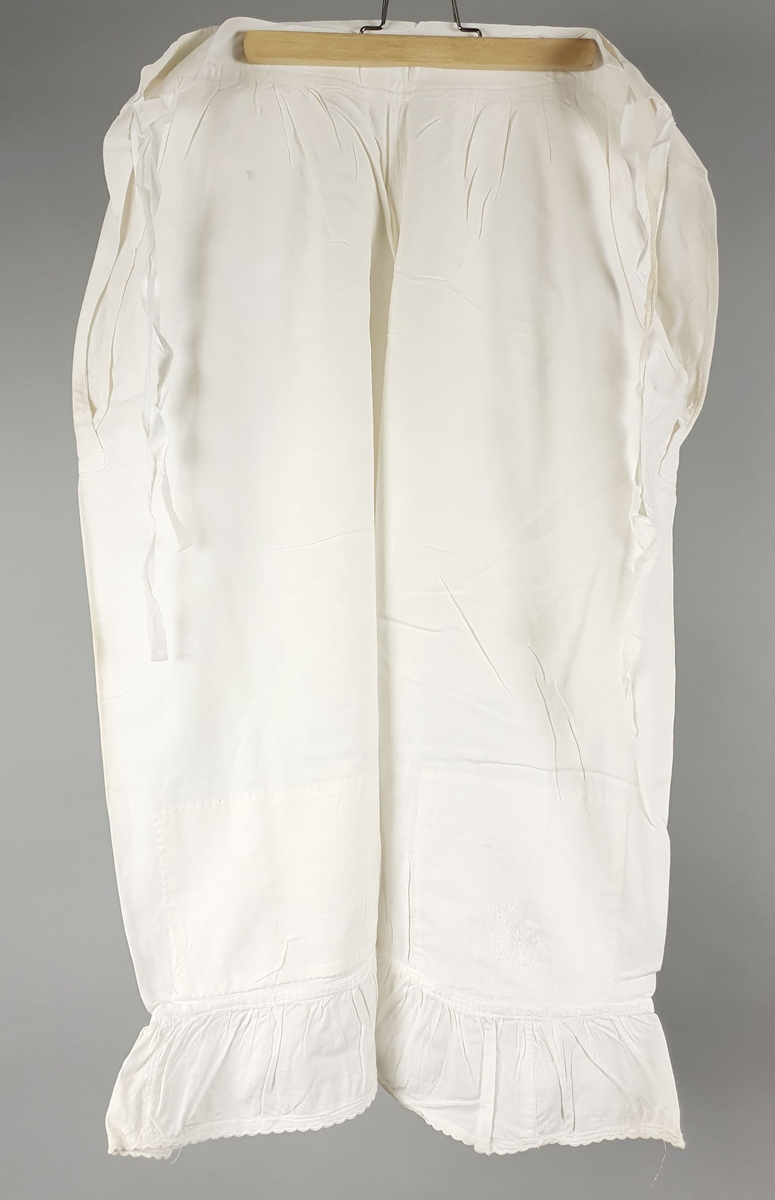 Ni like mamelukker med foldekant med bølget kant nederst.  Åpning i hver side med knytebånd.