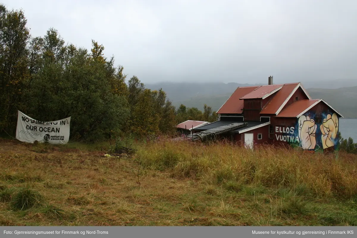 Protestleiren på Markoppneset i Finnmark i 2021. Protestbevegelsen mot dumping av gruveavfall i Repparfjorden har samlet seg og har etablert en teltleir. Bildet er del av en serie som dokumenterer leiren og omgivelsen i området.
Bildet på naustveggen er et verk av kunstneren Tegson og har tittelen "Ellos vuotna".