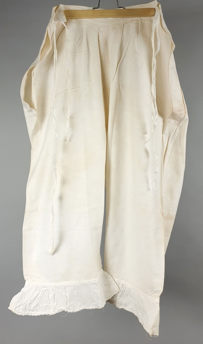 Ni like mamelukker med foldekant med bølget kant nederst.  Åpning i hver side med knytebånd.