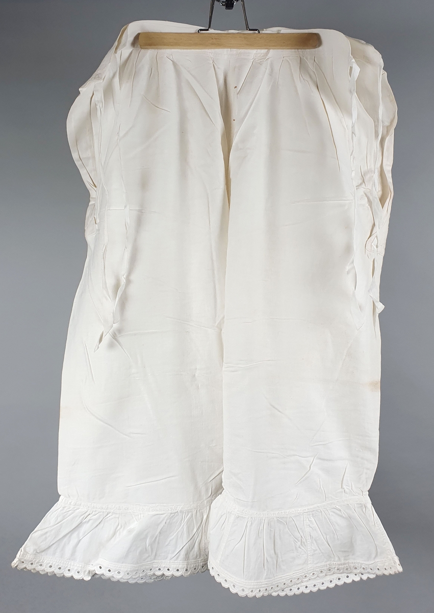 Ni like mamelukker med foldekant med bølget kant nederst.  Åpning i hver side med knytebånd.