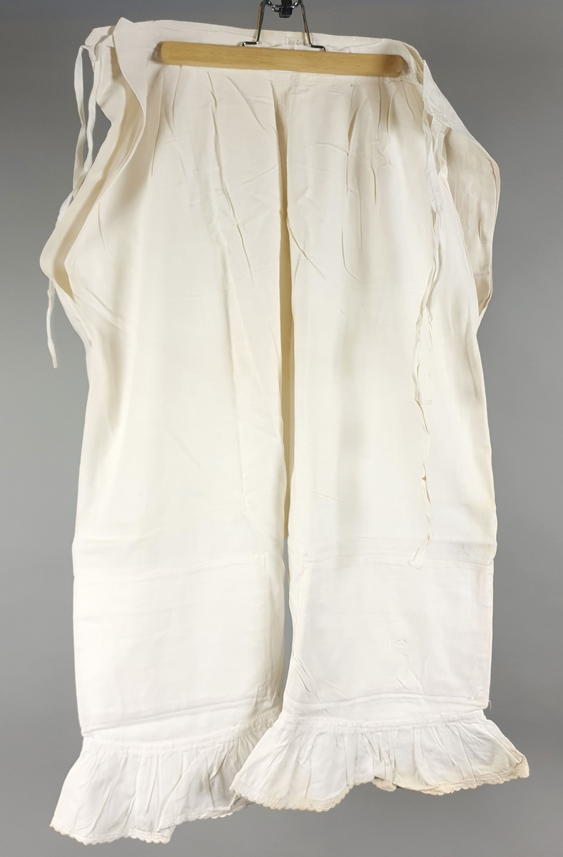 Ni like mamelukker med foldekant med bølget kant nederst.  Åpning i hver side med knytebånd.