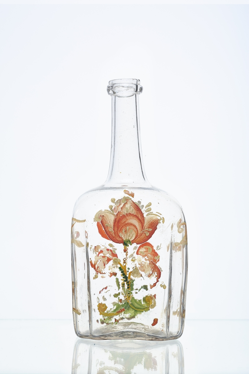 Blåst karaffel i blankt glass. Brutt puntelmerke i bunnen. Påmalt blomsterdekorasjon, med årstallet 1732 og bokstavene JT og DR. 1732 antas å være fødselsåret til eieren, da denne flasketypen kom seinere. 
