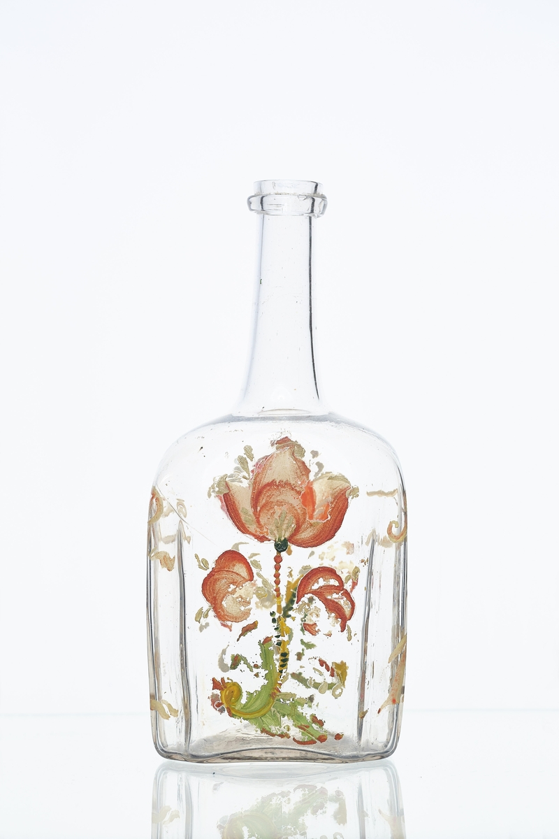 Blåst karaffel i blankt glass. Brutt puntelmerke i bunnen. Påmalt blomsterdekorasjon, med årstallet 1732 og bokstavene JT og DR. 1732 antas å være fødselsåret til eieren, da denne flasketypen kom seinere. 
