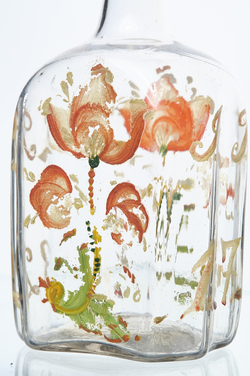 Blåst karaffel i blankt glass. Brutt puntelmerke i bunnen. Påmalt blomsterdekorasjon, med årstallet 1732 og bokstavene JT og DR. 1732 antas å være fødselsåret til eieren, da denne flasketypen kom seinere. 
