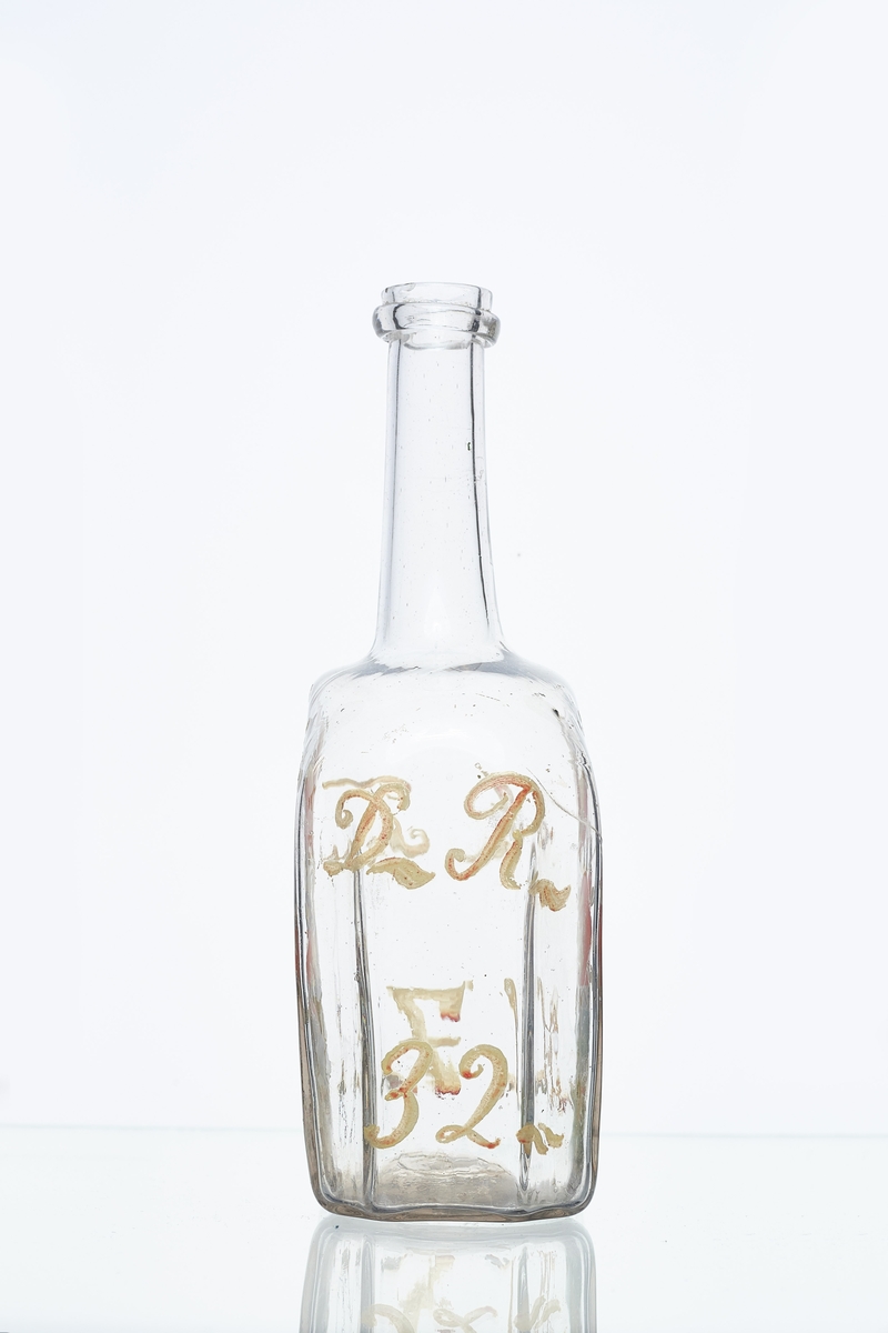 Blåst karaffel i blankt glass. Brutt puntelmerke i bunnen. Påmalt blomsterdekorasjon, med årstallet 1732 og bokstavene JT og DR. 1732 antas å være fødselsåret til eieren, da denne flasketypen kom seinere. 
