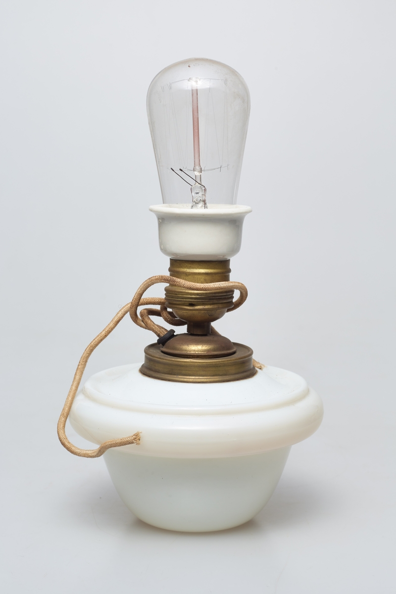 Heisbar parafinlampe ombygd for elektrisitet. Fra Høgbakken. Enkelstående med kuppel bunn i hvit porselen.  Det stikker ut ett tau ut av midten.