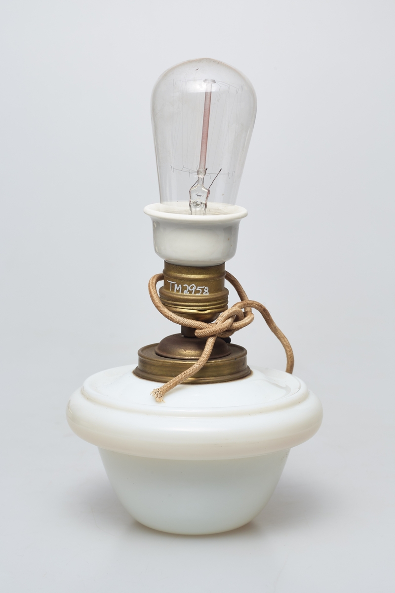 Heisbar parafinlampe ombygd for elektrisitet. Fra Høgbakken. Enkelstående med kuppel bunn i hvit porselen.  Det stikker ut ett tau ut av midten.