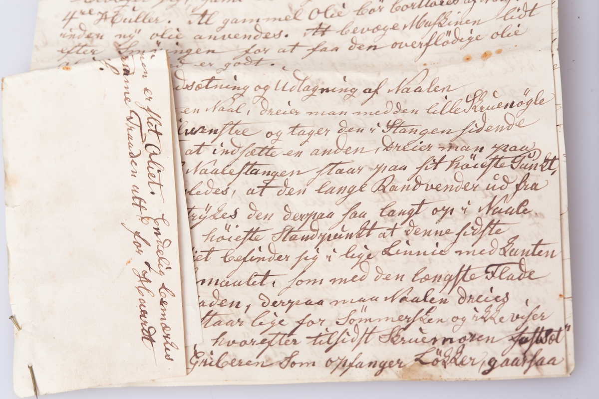 Symaskin for håndkraft. Symaskinen er enkelttrådet. Rødmalt kasse for symaskinen av gran med skyvelokk. I kassen ligger mange reservedeler og 3 nåler.  Noe er innpakket i avispapir fra 1899.