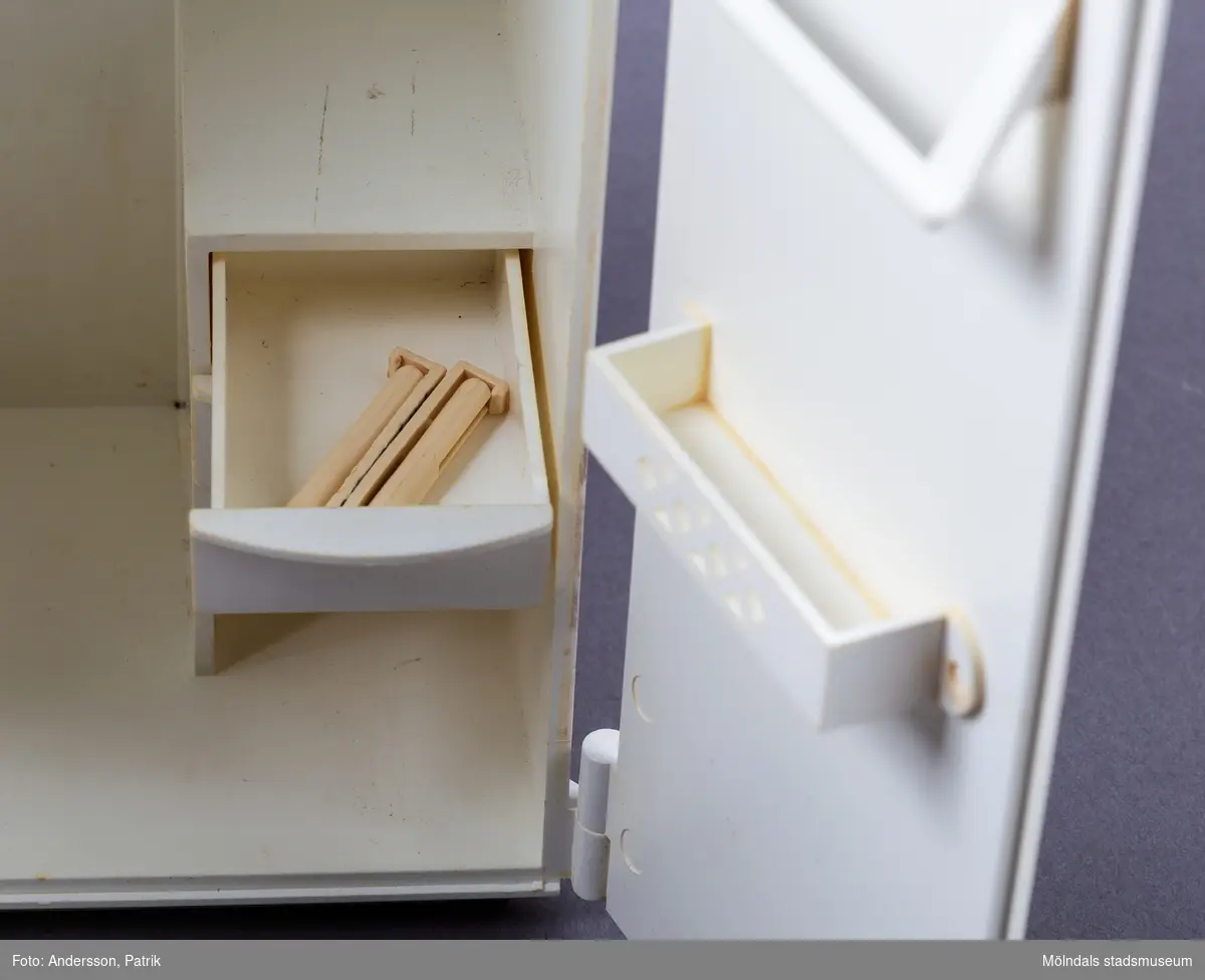 Vit leksaksgarderob med gulddekor. Till skåpet hör fem galgar och två papiljotter. 

Inuti garderoben finns en liten byrå med tre lådor (en låda saknas dock).  På insidan av den vänstra garderobsdörren finns en spegel och en skohylla. På den högra dörren finns en liten hylla och en stång för skärp och scarfs. 

Garderoben är ett tillbehör till dockan Sindy.

Sindy var en docka som tillverkades av ett stort antal företag på licens från Pedigree Dolls & Toys: Pedigree under åren 1963-1986, Hasbro 1987-1996, Funskool 1994-2006 samt Vivid Imaginations 1998-2003.