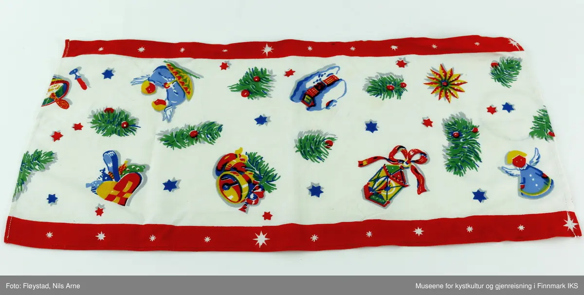 En rektangulær juleløper av bomull med maskinsøm langs kantene og trykt motiv. Duken har to røde dekorkanter med hvite stjerner på langsidene av duken. Motivet på duken består av små blå og røde stjerner og grønne grener med røde bær, i tillegg til bjeller, et hus, en lykt engler, en stor stjerne og en skål med grøt oppi helt i ene enden av duken. Fargene på duken er hvit, rød, grønn, gul og blå. 