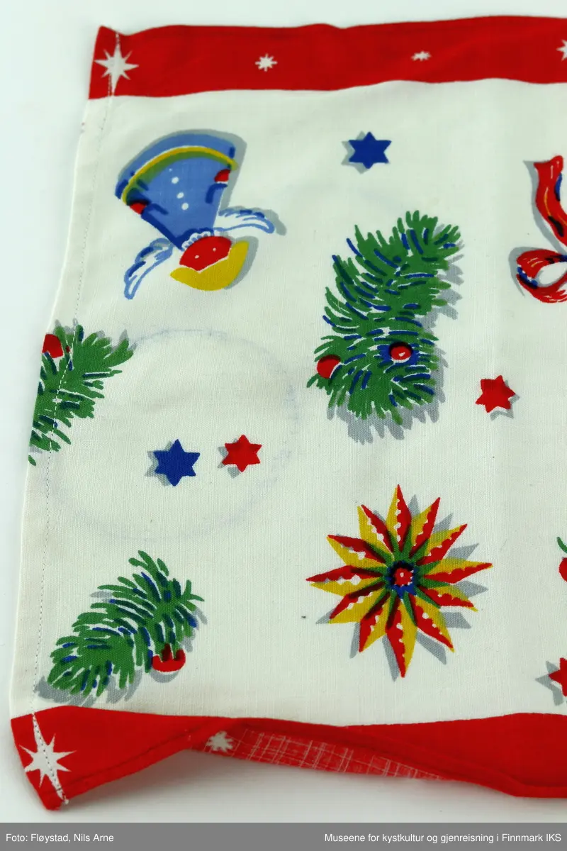 En rektangulær juleløper av bomull med maskinsøm langs kantene og trykt motiv. Duken har to røde dekorkanter med hvite stjerner på langsidene av duken. Motivet på duken består av små blå og røde stjerner og grønne grener med røde bær, i tillegg til bjeller, et hus, en lykt engler, en stor stjerne og en skål med grøt oppi helt i ene enden av duken. Fargene på duken er hvit, rød, grønn, gul og blå. 