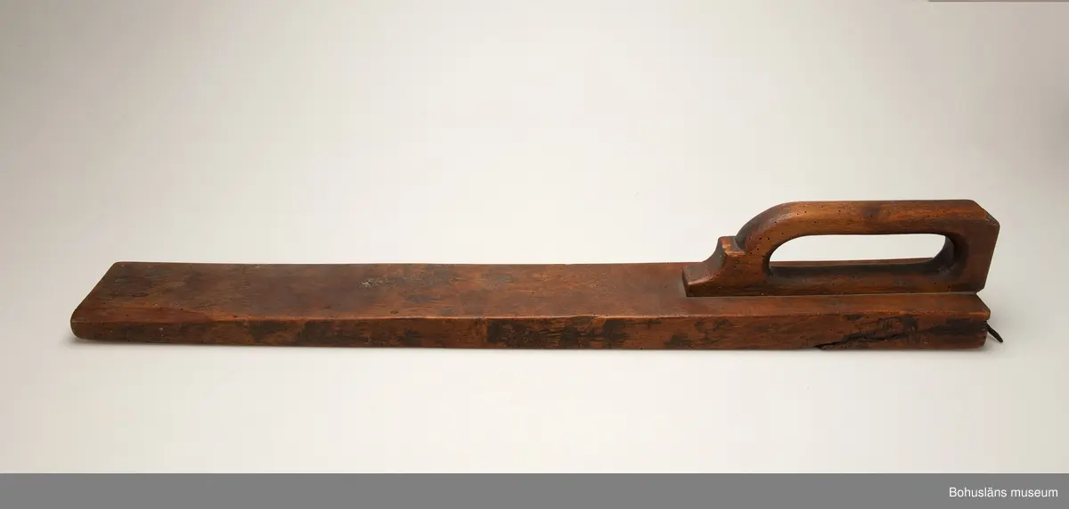 Platt, rektangulärt redskap med handtag inskjutet i ett spår.
Vid handtaget, på ovansidan, är årtalet "1822" och ägarinitialerna "I:E" inskurna.
Handtaget är profilerat framtill.
Betsen är något bortsliten på grund av användning.
Kavelrullen att linda tyget runt saknas.
Skadedjursangrepp.

Litteratur:
Fredlund, Jane. Stora boken om livet förr, ICA-förlaget, Västerås 1981, s. 40-49.

Kan sammanhöra med UM2392 (se läderbit, spik, bets).

Ur handskrivna katalogen 1957-1958:
Kavelträ "I: E" "1822"
MANGELBRÄDE L. 81,5. Br. 11. Trä. Obetydligt skadat. Maskhål. Stenungsund, Norum, Bohusl.

Lappkatalog: 72