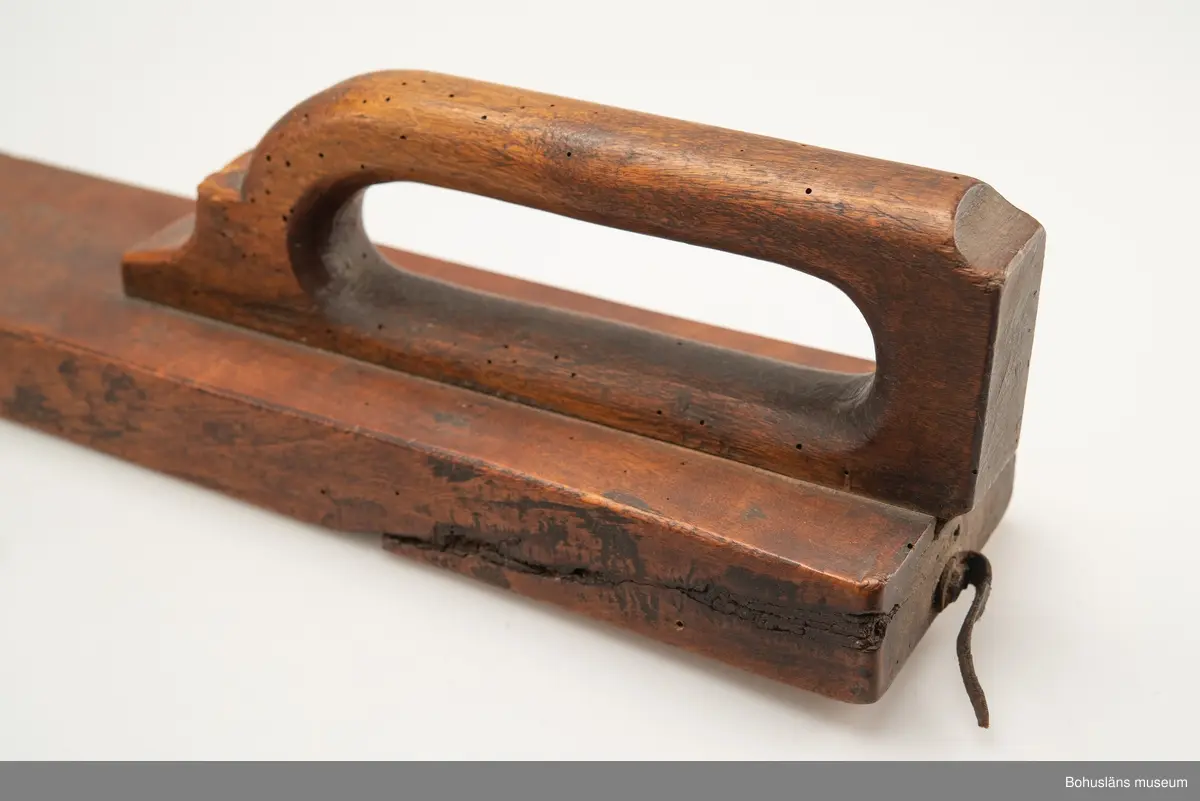 Platt, rektangulärt redskap med handtag inskjutet i ett spår.
Vid handtaget, på ovansidan, är årtalet "1822" och ägarinitialerna "I:E" inskurna.
Handtaget är profilerat framtill.
Betsen är något bortsliten på grund av användning.
Kavelrullen att linda tyget runt saknas.
Skadedjursangrepp.

Litteratur:
Fredlund, Jane. Stora boken om livet förr, ICA-förlaget, Västerås 1981, s. 40-49.

Kan sammanhöra med UM2392 (se läderbit, spik, bets).

Ur handskrivna katalogen 1957-1958:
Kavelträ "I: E" "1822"
MANGELBRÄDE L. 81,5. Br. 11. Trä. Obetydligt skadat. Maskhål. Stenungsund, Norum, Bohusl.

Lappkatalog: 72