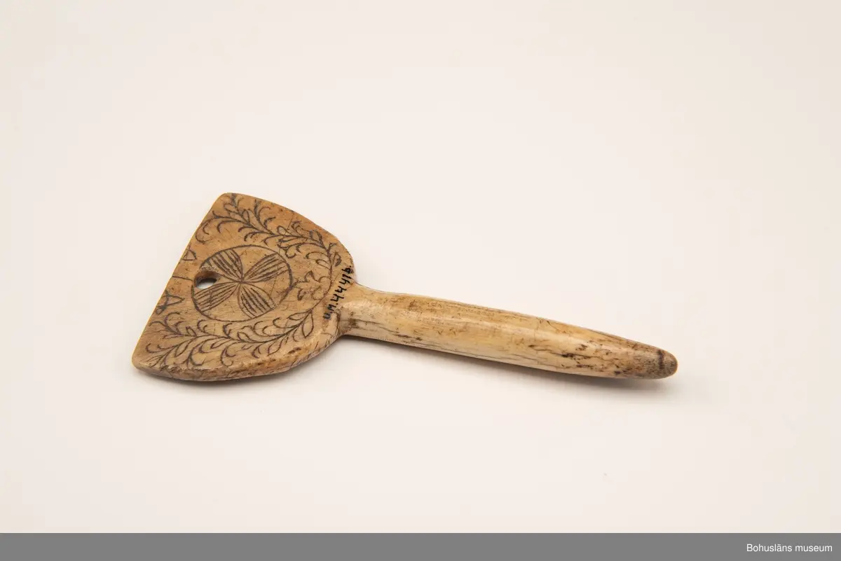 Rund pinne med triangulärliknande platta upptill. På en av sidorna finns ristad och svärtad dekor bestående av två korsade bladslingor med en rosett i mitten.
Baksidan har mörknat på grund av användning.

Ur handskrivna katalogen 1957-1958:
Två selpinnar av ben
b) Mått: 16,7 x 7,5 cm; form som föreg; dekoren har rankor och en stiliserad blomma. Hel.

Svar på förfrågan kring föremålen UM003945, UM004440, UM004441, UM004442 till Ajttemuseet, Jokkmokk januari 2007, som skriver:
Vi uppfattar inte föremålen som direkt samiska, inte heller i gravyren. Visst har det funnits bofasta samer, så det kan vara möjligt, men ofta hade de också renar för transport. 
Enligt Stig Harry Johansson, Tärnaby som besökte museet 17/3 1988 är föremålet tillverkat av horn från älg eller ren.

Lappkatalog: 40

Litt.; Nylén, Anna-Maja, Hemslöjd, Håkan Ohlssons förlag, Lund, 1978, s. 396-401.