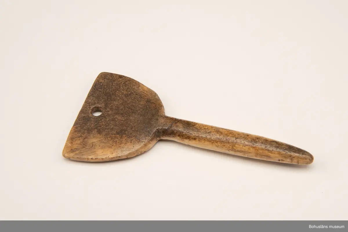 Rund pinne med triangulärliknande platta upptill. På en av sidorna finns ristad och svärtad dekor bestående av två korsade bladslingor med en rosett i mitten.
Baksidan har mörknat på grund av användning.

Ur handskrivna katalogen 1957-1958:
Två selpinnar av ben
b) Mått: 16,7 x 7,5 cm; form som föreg; dekoren har rankor och en stiliserad blomma. Hel.

Svar på förfrågan kring föremålen UM003945, UM004440, UM004441, UM004442 till Ajttemuseet, Jokkmokk januari 2007, som skriver:
Vi uppfattar inte föremålen som direkt samiska, inte heller i gravyren. Visst har det funnits bofasta samer, så det kan vara möjligt, men ofta hade de också renar för transport. 
Enligt Stig Harry Johansson, Tärnaby som besökte museet 17/3 1988 är föremålet tillverkat av horn från älg eller ren.

Lappkatalog: 40

Litt.; Nylén, Anna-Maja, Hemslöjd, Håkan Ohlssons förlag, Lund, 1978, s. 396-401.