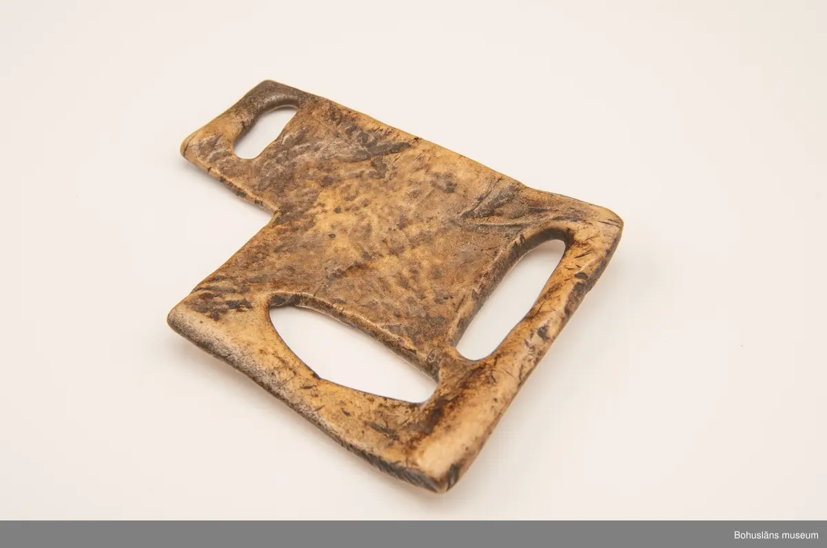 Skiva med tre avlånga urtag att fästa remmar i.
Mittpå en av sidorna är siffrorna "1119" inristade (kan vara år-talet "1779"?).
Har mörknat på grund av användning.

Ur handskrivna katalogen 1957-1958:
Remskiva av ben (för seldon)
Mått: 15,5 x 11 cm; (teckning) 3 fästen f. remmar; "1119". Hel.

Svar på förfrågan kring föremålen UM003945, UM004440, UM004441, UM004442 till Ajttemuseet, Jokkmokk januari 2007, som skriver:
Vi uppfattar inte föremålen som direkt samiska, inte heller i gravyren. Visst har det funnits bofasta samer, så det kan vara möjligt, men ofta hade de också renar för transport. 
Enligt Stig Harry Johansson, tärnaby som besökte museet 17/3 1988 är föremålet tillverkat av älg eller renhorn.

Lappkatalog: 40

Litt.; Nylén, Anna-Maja, Hemslöjd, Håkan Ohlssons förlag, Lund, 1978, s. 396-401.