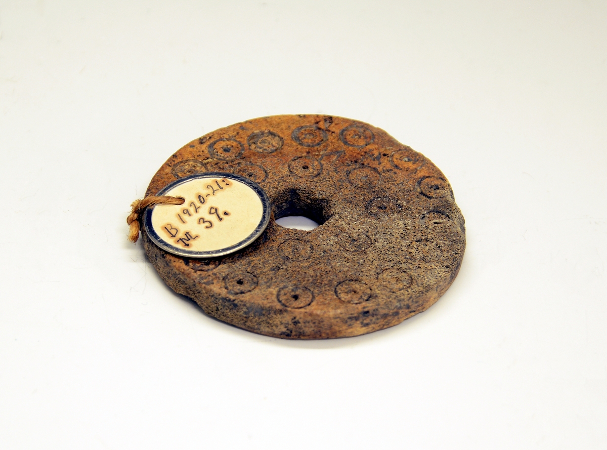 Skiveformet spinnehjul til håndtein. Fra protokollen: Spinnehjul av bein, 3/4 cm. tykt. Knivbora hol i midten. Prydt med 2 koncentriske ringar med cirkelornament, paa baae sidur. (R. Berge)