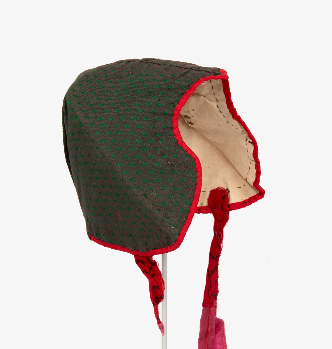 Mössa, mjuk bindmössa till Svärdsjö sockendräkt för kvinna. Av bomullstyg, brun/grön botten med små gröna mönsterprickar. Baktill ett veck på var sida om mittsömmen. Snibb mitt fram. Kantad med rött sidenband. Mellanlägg av lin. Fodrad med oblekt bomullslärft. Knytband av rött bomullstyg och rosa band.