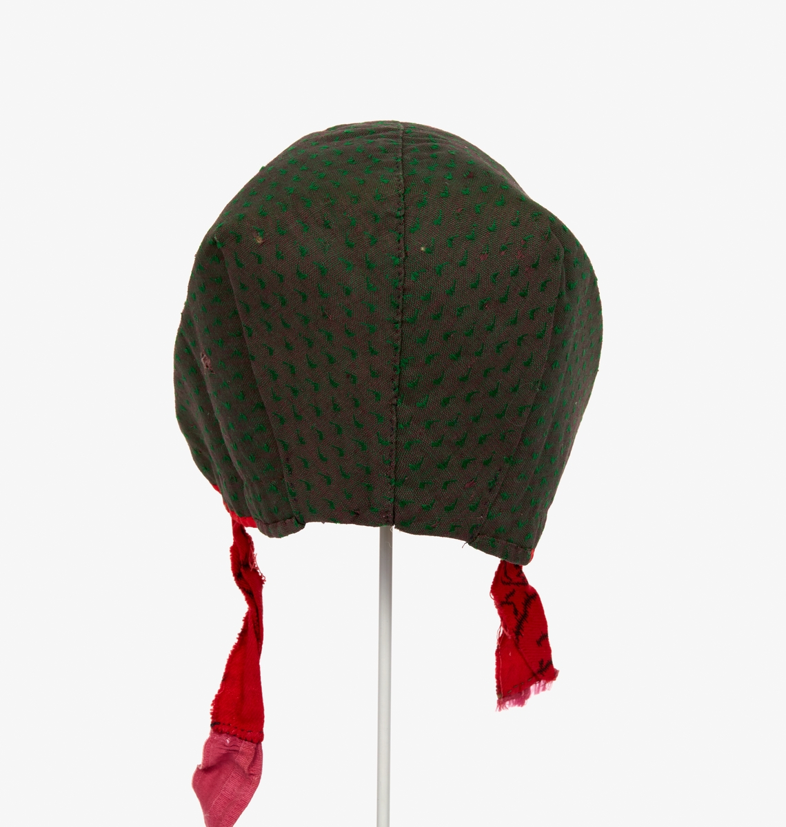 Mössa, mjuk bindmössa till Svärdsjö sockendräkt för kvinna. Av bomullstyg, brun/grön botten med små gröna mönsterprickar. Baktill ett veck på var sida om mittsömmen. Snibb mitt fram. Kantad med rött sidenband. Mellanlägg av lin. Fodrad med oblekt bomullslärft. Knytband av rött bomullstyg och rosa band.