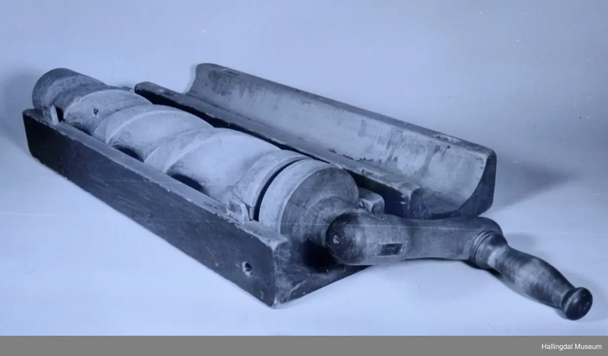 Avlang kasseform, svakt skrånende sider. Består av to deler tappet sammen. Sylindrisk hull gjennom kassen på langs, til valsen. Grove riller på valsen. Oppå kassen kvadratisk hull ned til valsen. Rødmalt.
23/6-67 O. Foldøy.