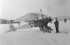 Flygplan Thulin D nr 15 i vintermålning på Flygkompaniet på Malmen, 1917. Två mekaniker står vid flygplanet.