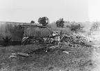 Ett militärt havererat flygplan ligger på ett fält, 1920-tal. Flygplanet har antagligen brunnit.
