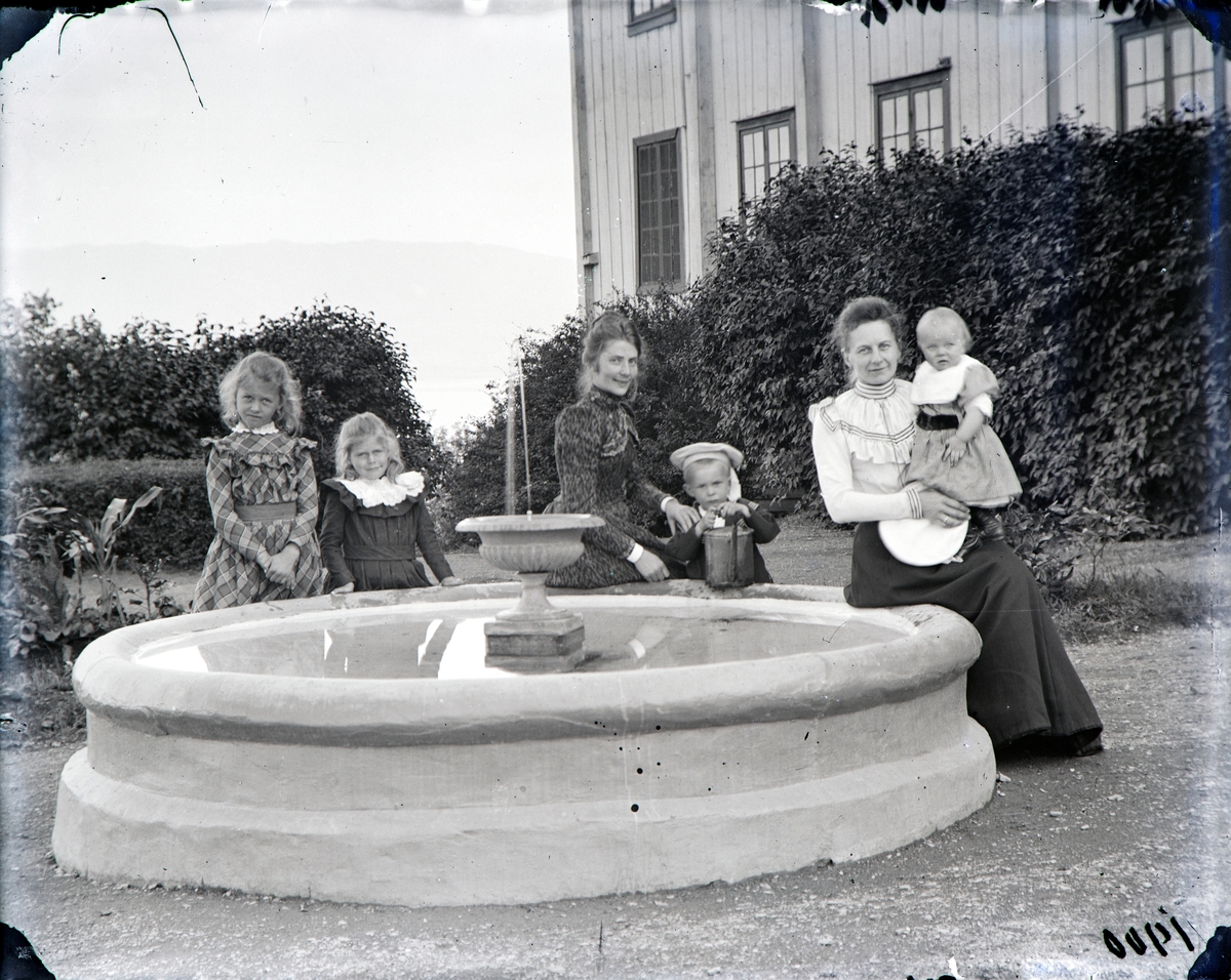 Samling rundt vannfontenen i hagen på Hovinsholm 1900. 
Fra v.: Martha Louise Hoel, Thora Hoel, barnepike Cecilie ? med Reidar Ramm Boe, og Marie Kobberstad g. Hoel med Jacob Hoel, 1 år.