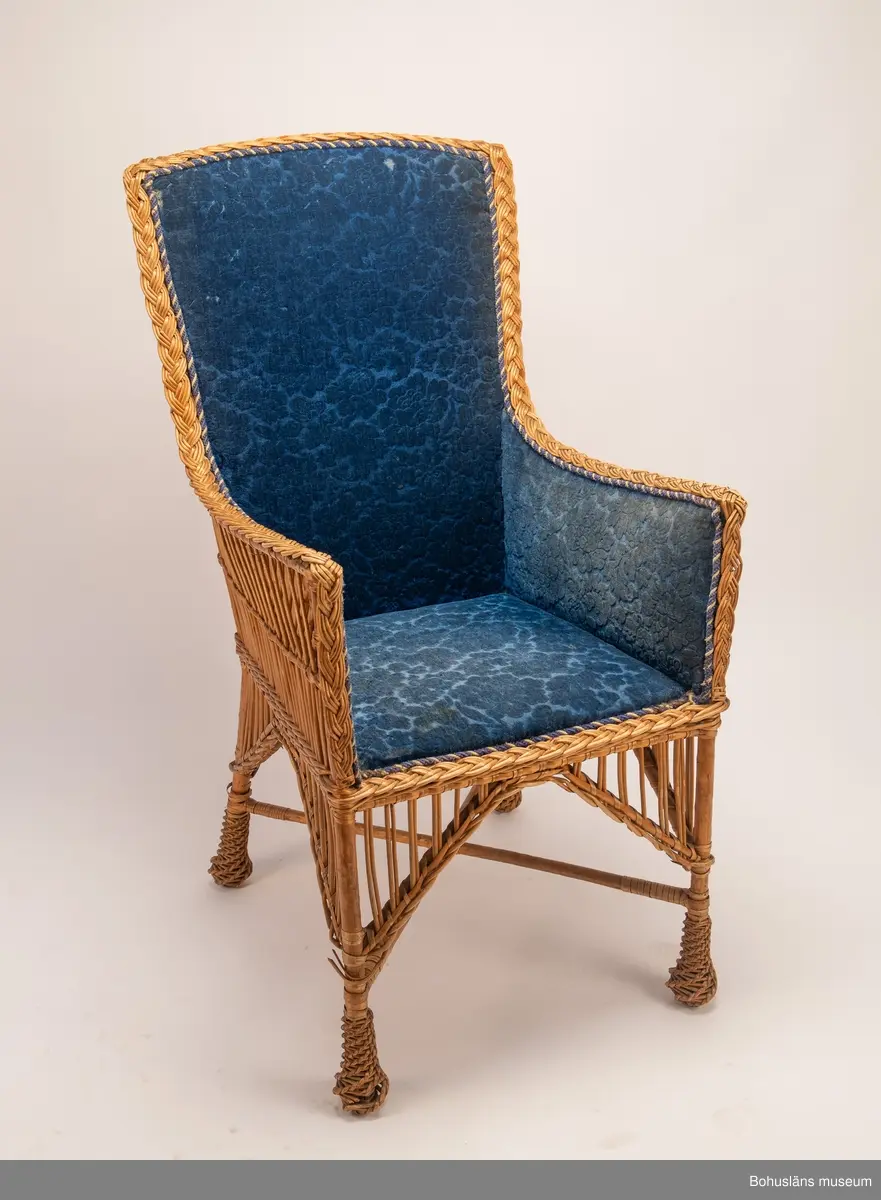 Ur handskrivna katalogen 1957-1958:
Korgstol
H. 117; Br. 59 cm; sits, ryggstöd och armstöd är på "insidan" klädda m. blå, mönstrad plysch. Hel. 
Enligt Brander [Evert Brander, vaktmästare på Uddevalla museum under 1940- och 1950-talen] gjord för Oskar II till Uddevalla - Lelångebanans invigning.