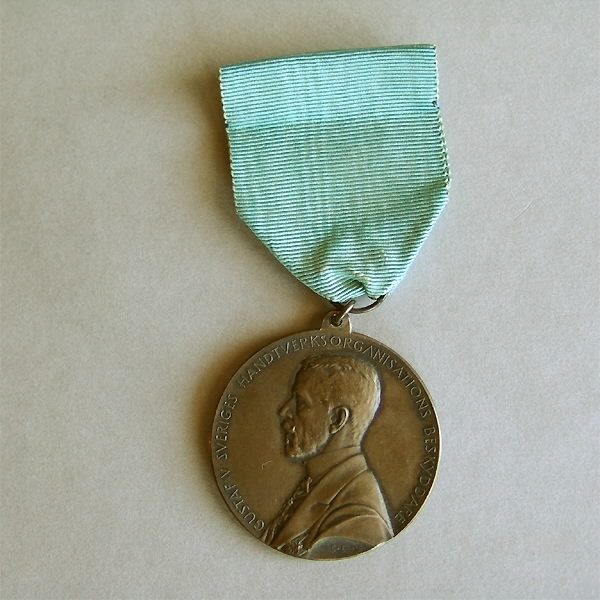 Rund medalj, försilvrad. Diameter 4 cm. Medaljen är fastsatt i ett blått sidenband. Framsida: Gustav V i profil samt text: "GUSTAV V SVERIGES HANTVERKSORGANISATIONS BESKYDDARE". Baksida: Kvinna knytande en krans, sittande på en tron. En sköld med tre kronor samt text: "TILL YRKENAS FÖRKOFRAN OSCAR DAHLBERG 1939". En säkerhetsnål fastsydd på sidenbandets baksida.
