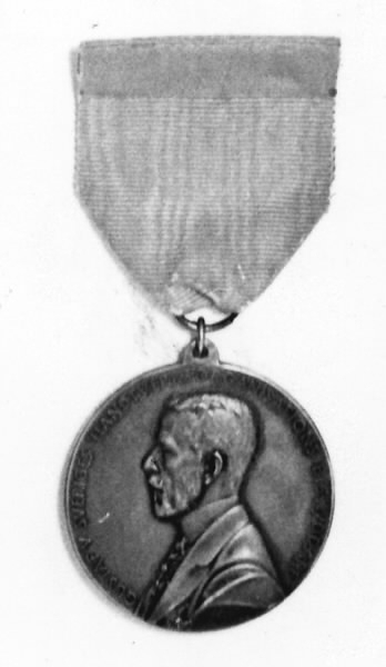 Rund medalj, försilvrad. Diameter 4 cm. Medaljen är fastsatt i ett blått sidenband. Framsida: Gustav V i profil samt text: "GUSTAV V SVERIGES HANTVERKSORGANISATIONS BESKYDDARE". Baksida: Kvinna knytande en krans, sittande på en tron. En sköld med tre kronor samt text: "TILL YRKENAS FÖRKOFRAN OSCAR DAHLBERG 1939". En säkerhetsnål fastsydd på sidenbandets baksida.
