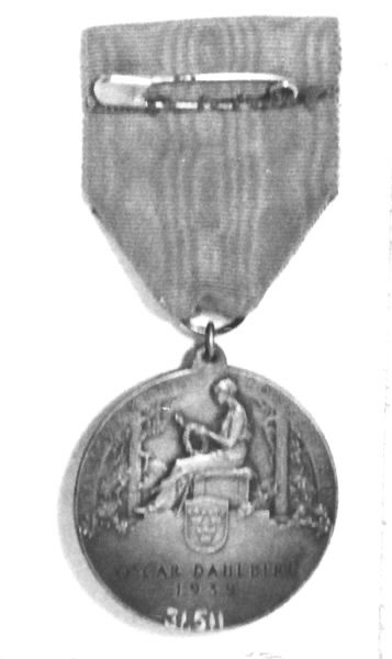 Rund medalj, försilvrad. Diameter 4 cm. Medaljen är fastsatt i ett blått sidenband. Framsida: Gustav V i profil samt text: "GUSTAV V SVERIGES HANTVERKSORGANISATIONS BESKYDDARE". Baksida: Kvinna knytande en krans, sittande på en tron. En sköld med tre kronor samt text: "TILL YRKENAS FÖRKOFRAN OSCAR DAHLBERG 1939". En säkerhetsnål fastsydd på sidenbandets baksida.